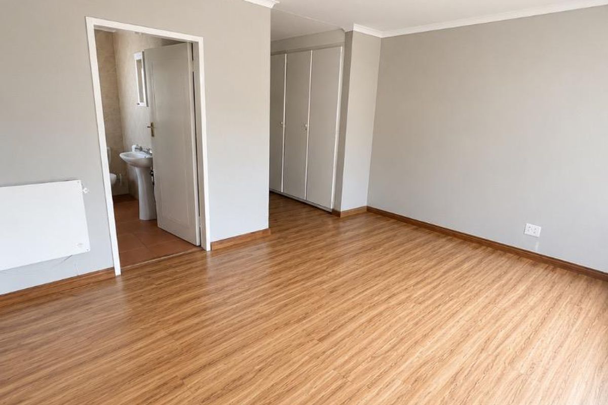 A spacious, empty bedroom featuring light wood-look laminate flooring, built-in cupboards, and an adjoining bathroom entrance.