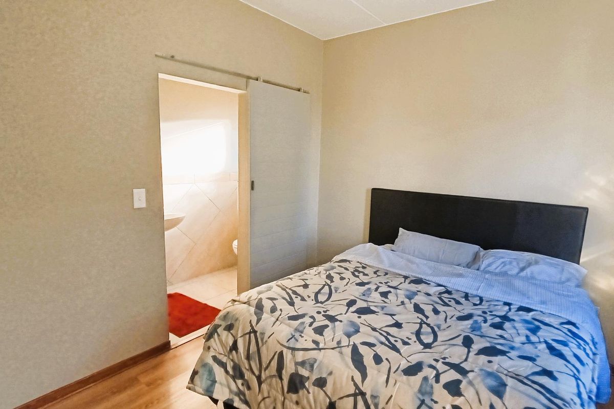 A bedroom featuring laminate flooring and a sliding door providing access to an en-suite bathroom.