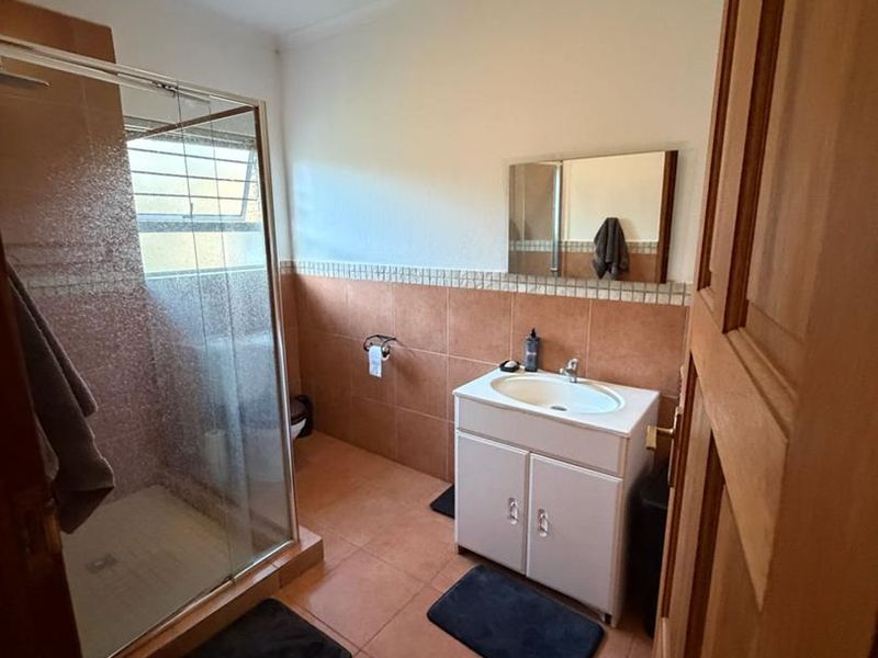 A functional bathroom featuring a glass-enclosed shower, a vanity unit with a basin, and neutral tiled finishes throughout.
