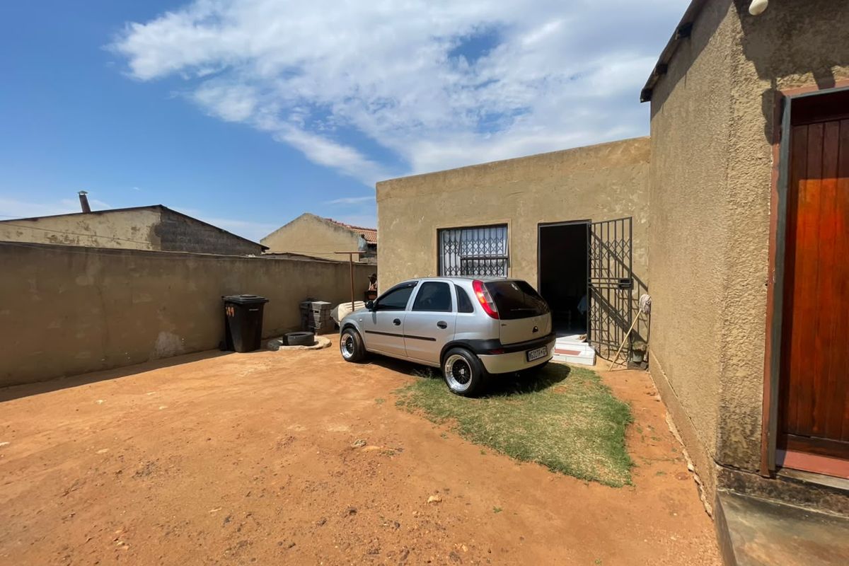 Rear exterior view of the property featuring a large unpaved yard area, perimeter wall, and security gate access to the main building.