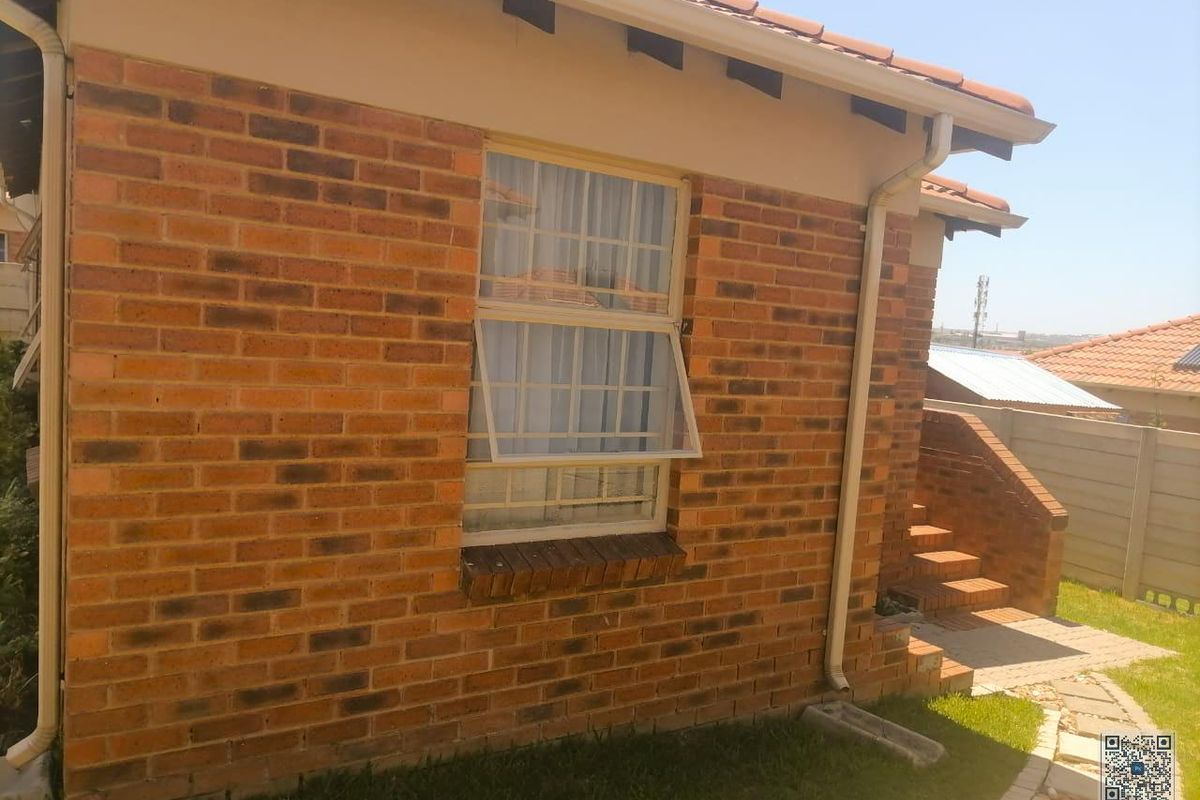 A side view of the house featuring face-brick exterior walls, a tiled roof, and a window with security bars.
