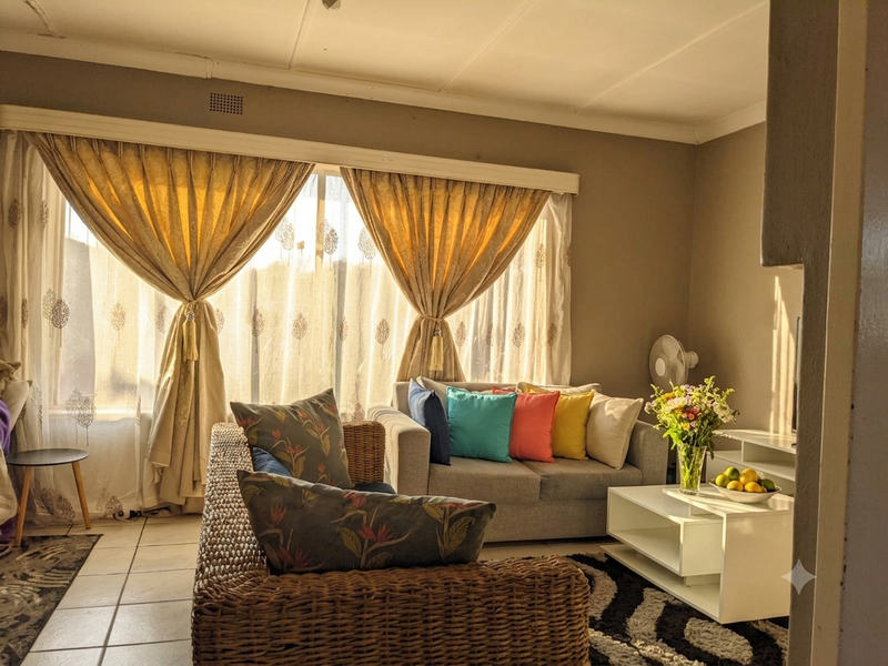 A sunlit living room featuring tiled flooring and a large window with curtain treatments, offering a comfortable and bright living space.