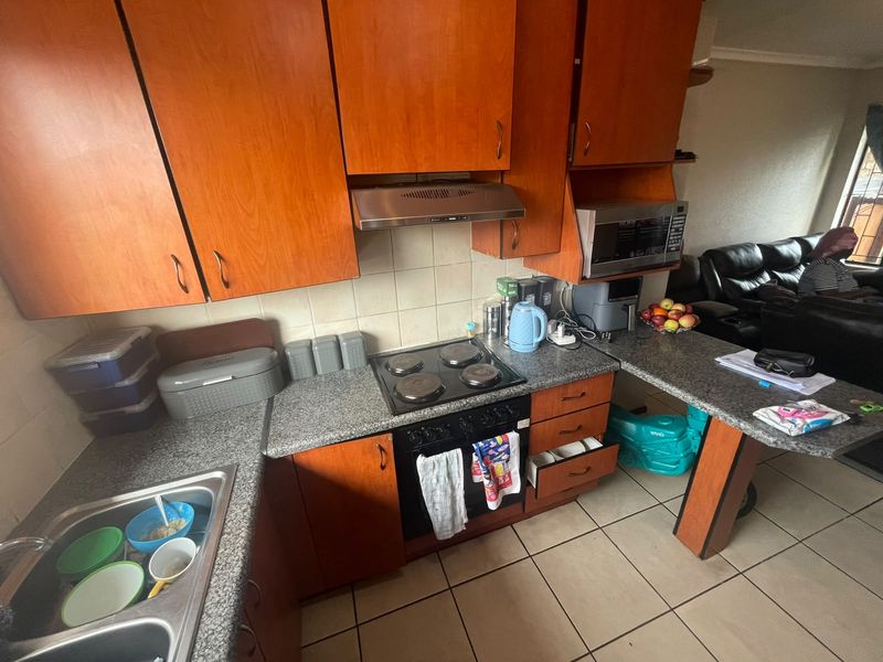 A functional kitchen featuring wood-tone cabinetry, granite countertops, a built-in oven with hob, and tiled flooring, offering a practical layout for daily meal preparation.