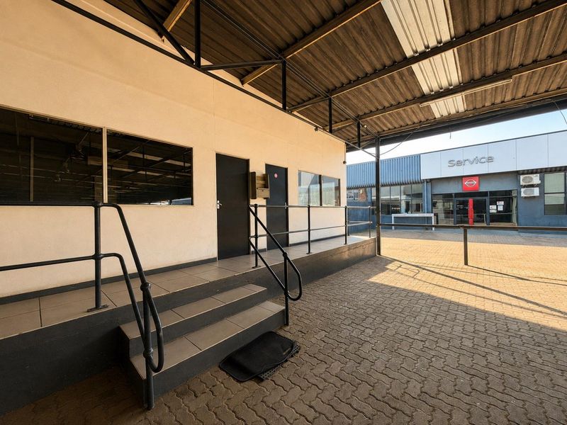A covered outdoor walkway with paved flooring, metal handrails, and tiled steps leading to building entrances in a commercial or mixed-use setting.