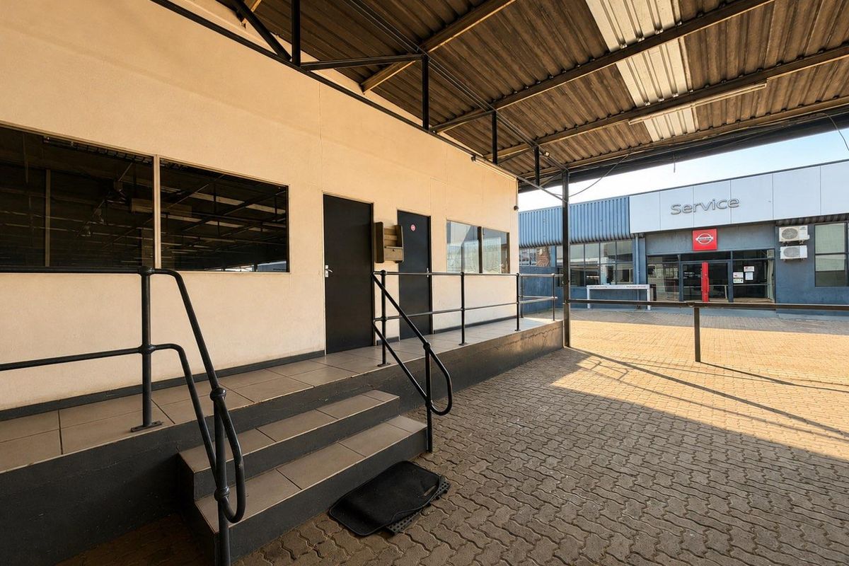 A covered outdoor walkway with paved flooring, metal handrails, and tiled steps leading to building entrances in a commercial or mixed-use setting.