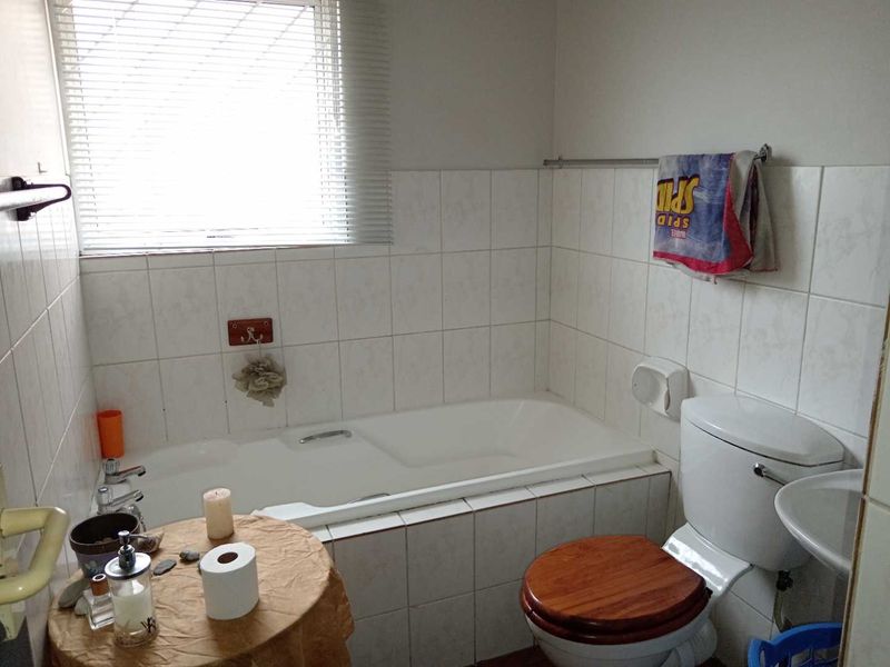 A functional bathroom featuring a built-in bathtub, pedestal basin, and toilet, finished with white ceramic wall tiles and fitted with venetian blinds.