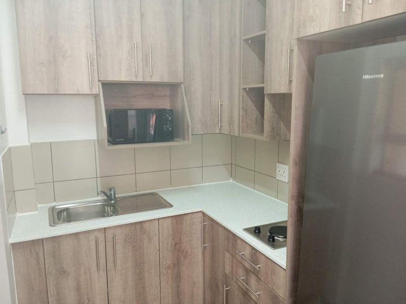 A compact, modern kitchen featuring wood-grain laminate cabinetry, a stainless steel sink, built-in hob, and neutral tiled splashback.