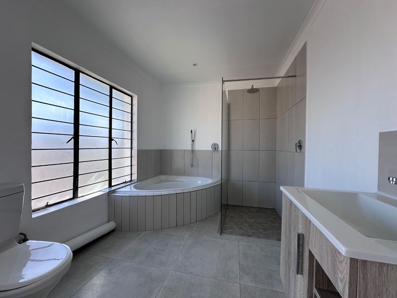 Modern bathroom featuring a corner bathtub, walk-in shower with glass screen, vanity cabinet, and neutral floor-to-ceiling tiling.