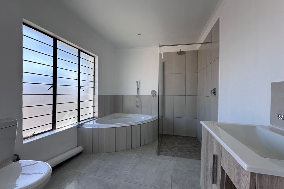Modern bathroom featuring a corner bathtub, walk-in shower with glass screen, vanity cabinet, and neutral floor-to-ceiling tiling.