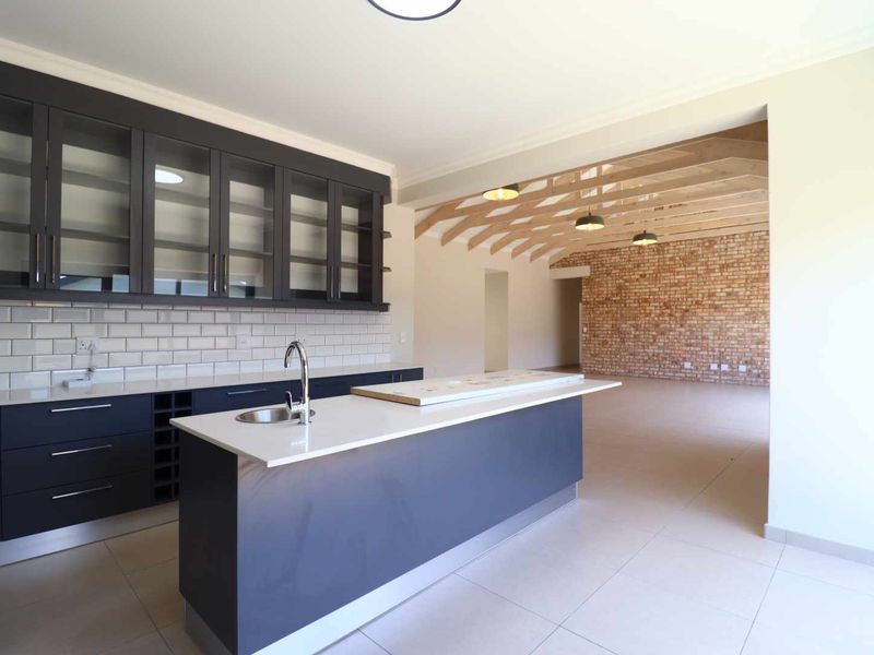 Modern open-plan kitchen featuring dark cabinetry, quartz countertops, subway tile backsplash, and a seamless transition to a living area with exposed brick and timber beams.