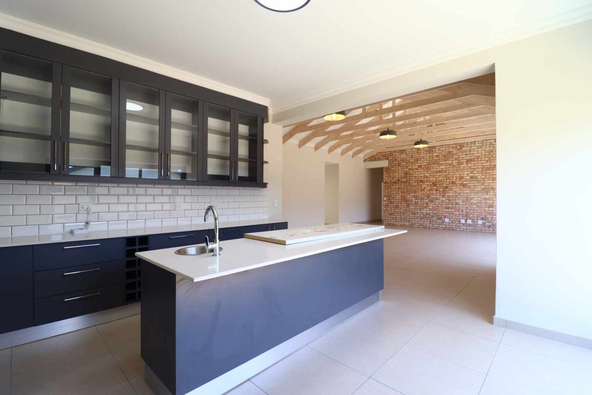 Modern open-plan kitchen featuring dark cabinetry, quartz countertops, subway tile backsplash, and a seamless transition to a living area with exposed brick and timber beams.