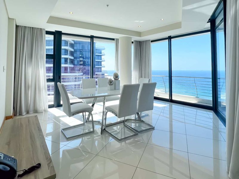 Bright and modern dining area featuring floor-to-ceiling windows with expansive ocean views and sleek tiled flooring.