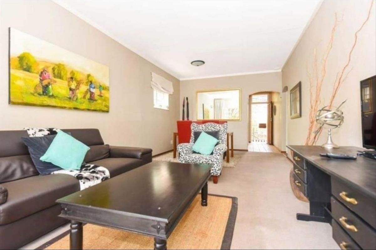 A comfortable living room area featuring neutral wall tones, carpeted flooring, and an archway leading to the entrance.
