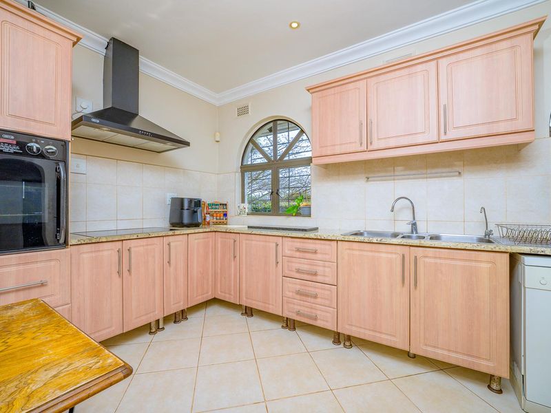 A functional kitchen featuring light wood cabinetry, granite countertops, a double bowl sink, built-in oven, and an extractor fan with distinctive arched windows.