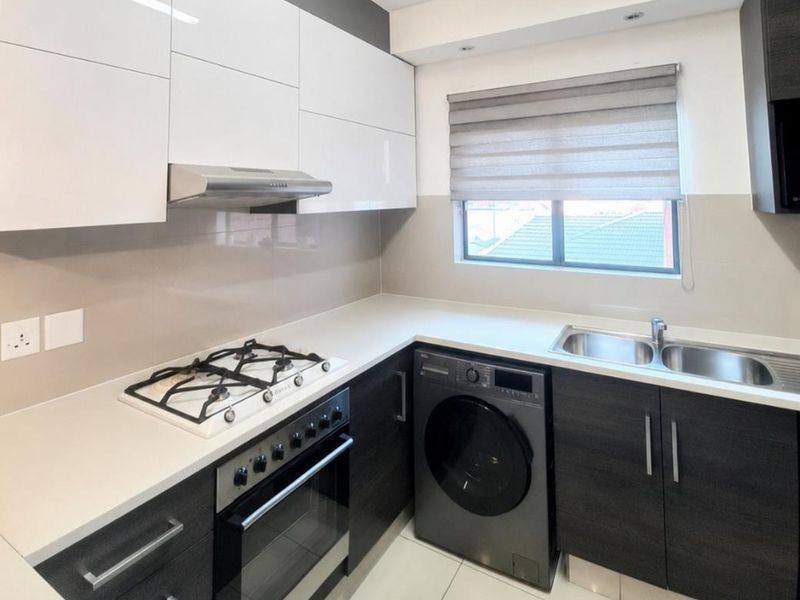 Modern kitchen featuring high-gloss cabinetry, stone countertops, gas hob, built-in oven, and integrated sink with neutral tiled flooring.