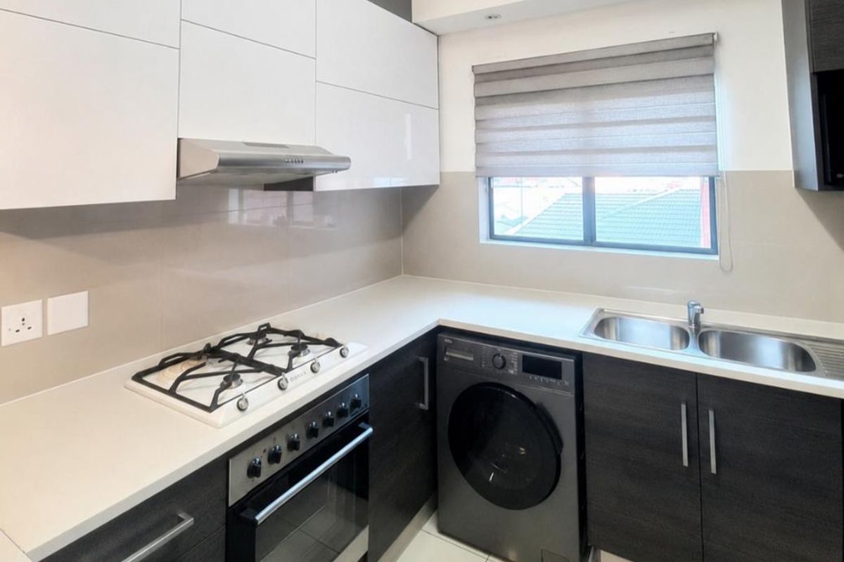 Modern kitchen featuring high-gloss cabinetry, stone countertops, gas hob, built-in oven, and integrated sink with neutral tiled flooring.