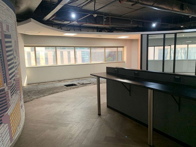 An open-plan office space featuring herringbone flooring, a built-in desk, and glass partitions, currently in a state of partial renovation.