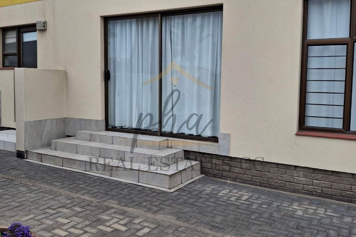 Rear exterior view of the townhouse featuring a paved patio area, sliding glass doors, and stone-tiled steps leading into the residence.