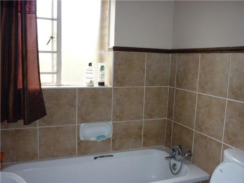 A functional bathroom featuring a bathtub with chrome fixtures, ceramic wall tiling, and a window with security bars.