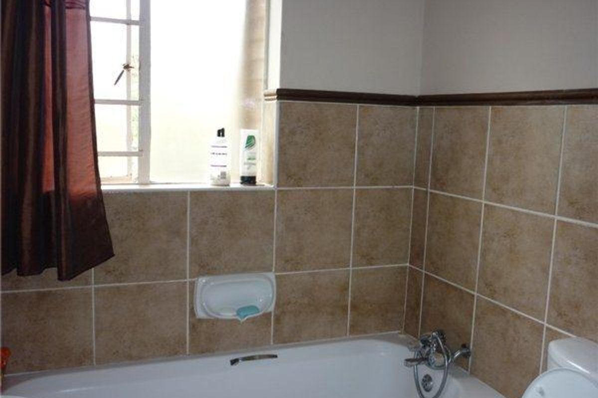 A functional bathroom featuring a bathtub with chrome fixtures, ceramic wall tiling, and a window with security bars.