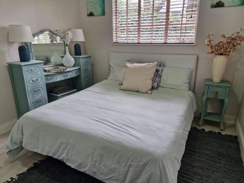 A cozy bedroom featuring tiled flooring, neutral walls, and a window fitted with venetian blinds, providing natural light and a comfortable living space.