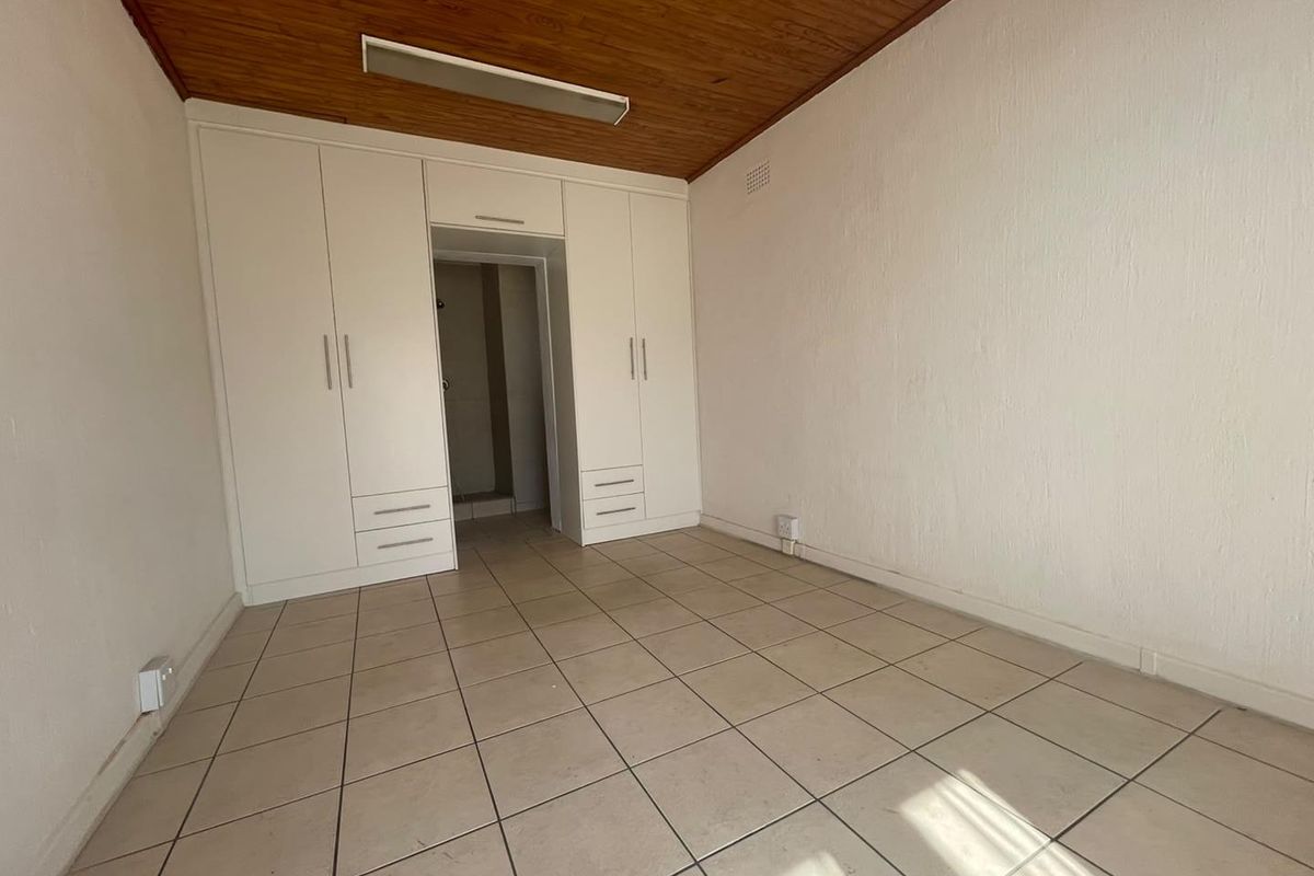 An empty bedroom featuring built-in cupboards, tiled flooring, and a timber-paneled ceiling, offering a blank canvas for renovation.