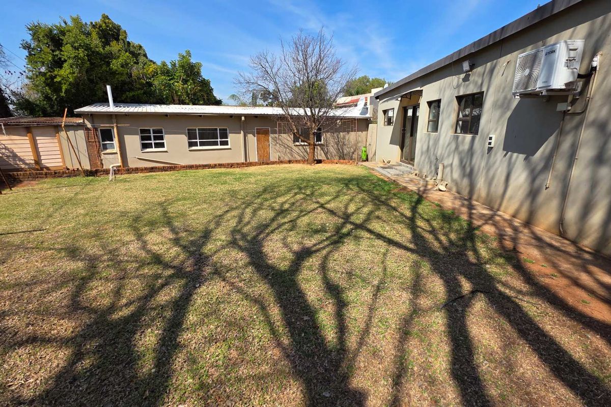 A spacious rear garden area featuring a lawn, exterior wall access, and an installed air conditioning unit on the side of the house.