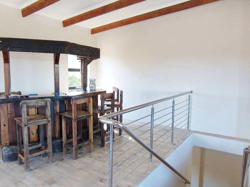 An elevated bar area featuring a rustic timber bar counter, exposed ceiling beams, and a modern stainless steel balustrade overlooking the lower level.