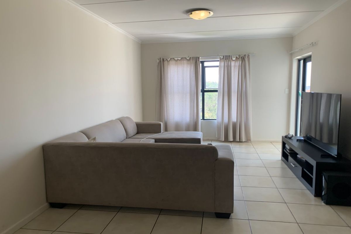 A bright and spacious living room featuring neutral tiled flooring, large windows with natural light, and a clean, minimalist layout.