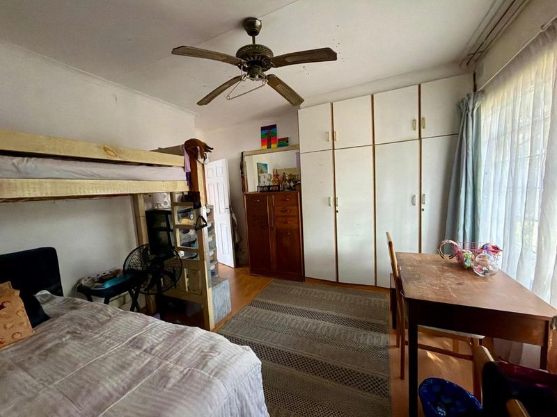 A bedroom featuring built-in cupboards, a ceiling fan, and laminate flooring, offering a functional space with potential for cosmetic updates.