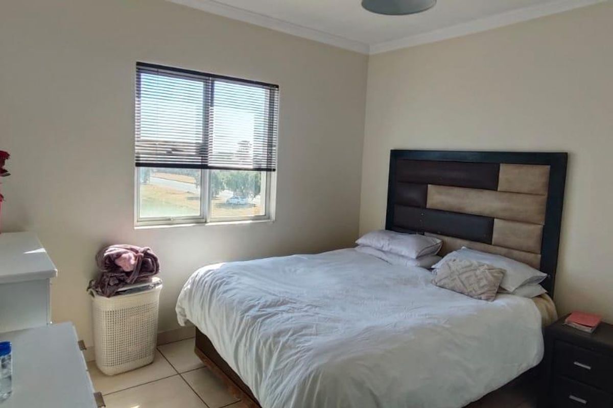 A functional bedroom featuring tiled flooring, a window with fitted venetian blinds, and built-in cupboard storage.