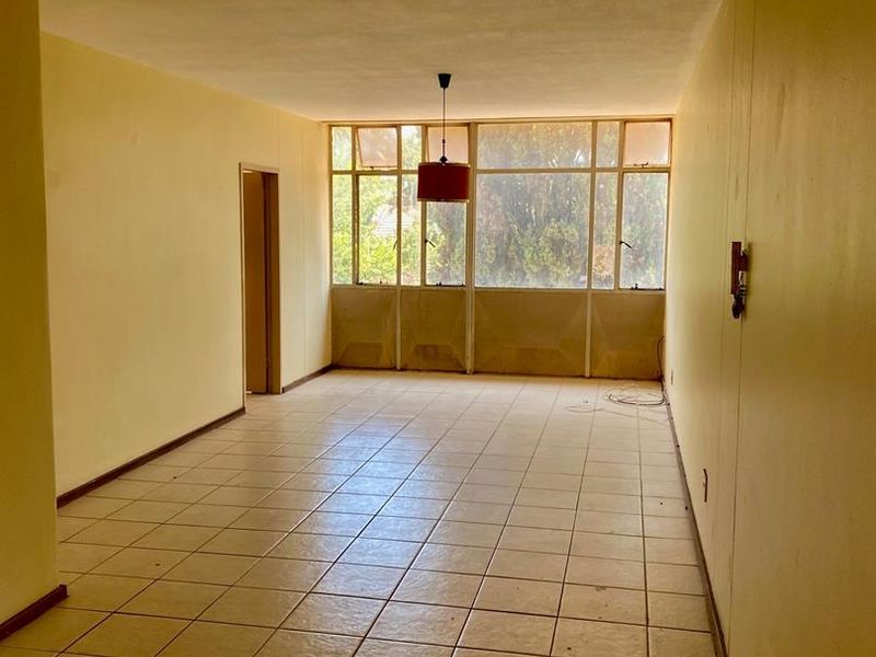 An empty, open-plan living area featuring tiled flooring and a large window wall, offering a blank canvas for renovation and interior design.