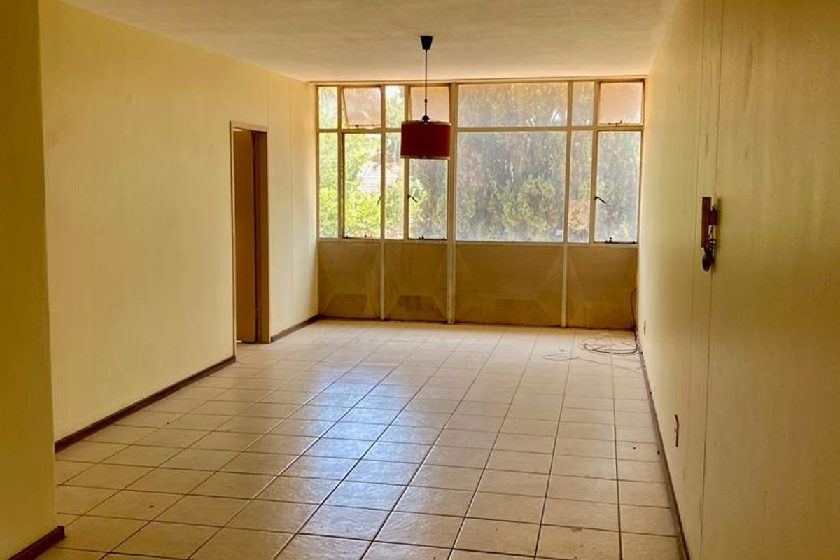 An empty, open-plan living area featuring tiled flooring and a large window wall, offering a blank canvas for renovation and interior design.