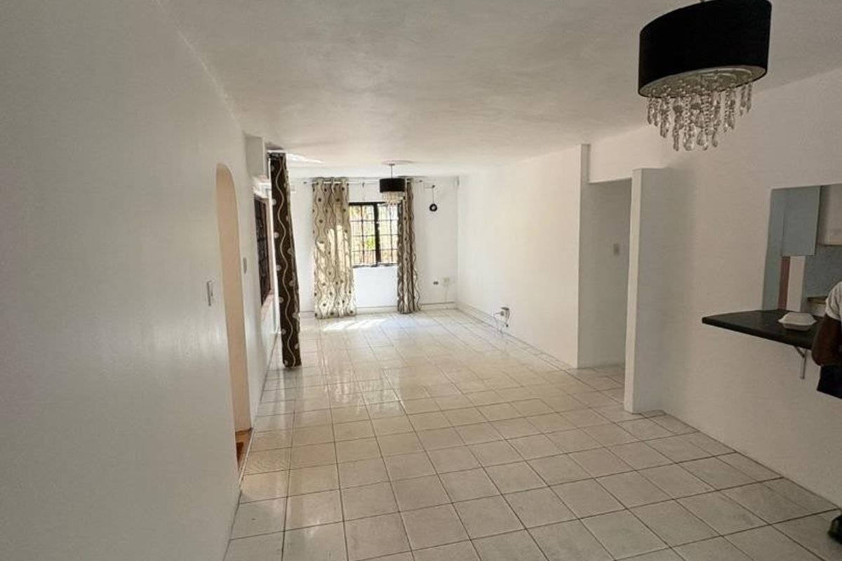 A spacious, open-plan living area featuring neutral tiled flooring, a breakfast bar, and an archway leading to adjacent rooms.