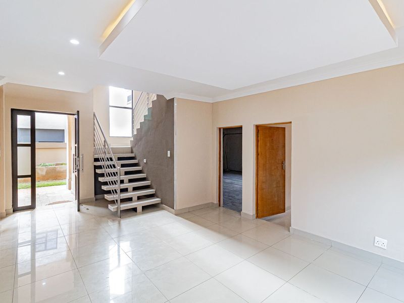Spacious open-plan living area featuring modern tiled flooring, a contemporary staircase, recessed ceiling lighting, and direct access to the exterior.