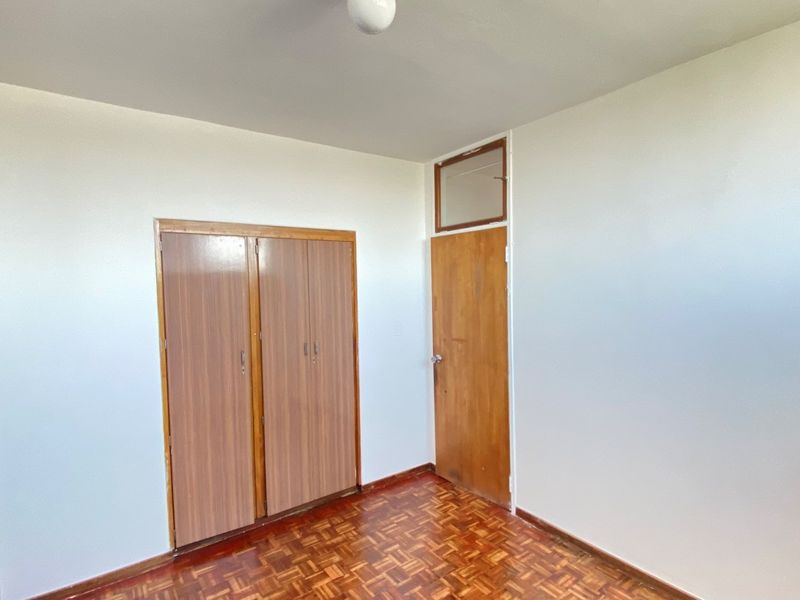 An empty bedroom featuring classic parquet flooring, built-in wooden cupboards, and a traditional wooden door with a transom window above.