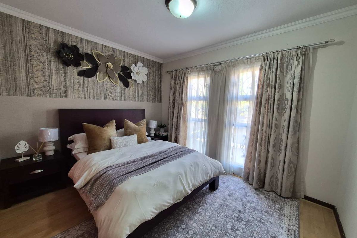 A well-lit bedroom featuring laminate flooring, crown molding, and a large window with curtain tracks, providing a comfortable and functional living space.