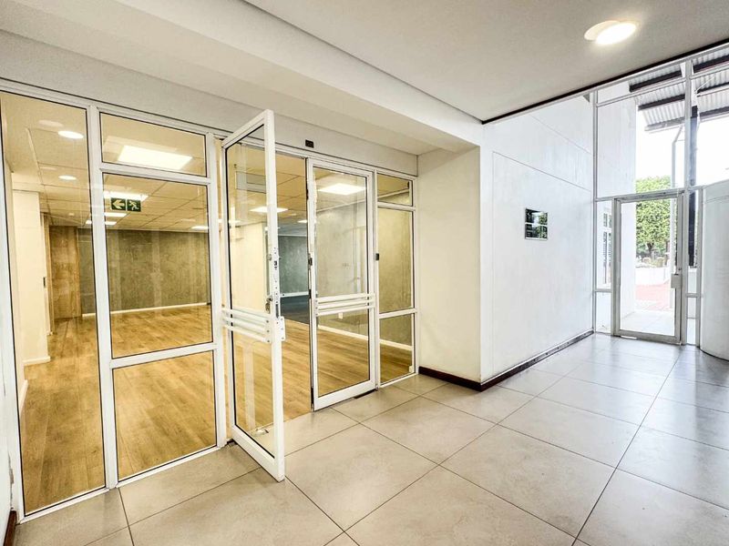 A bright, modern commercial entrance lobby featuring large glass partitions, tiled flooring, and clean white walls leading into an open-plan office space.