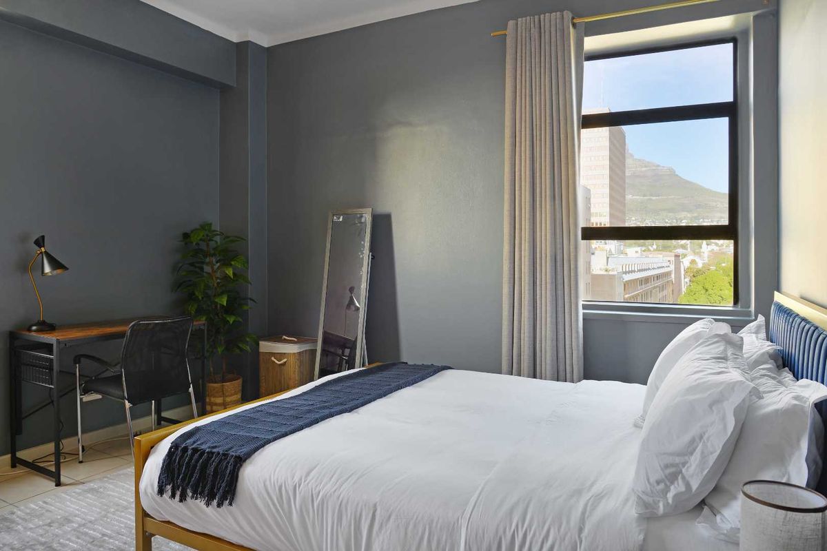 A well-maintained bedroom featuring neutral grey walls, tiled flooring, and a large window offering urban views.