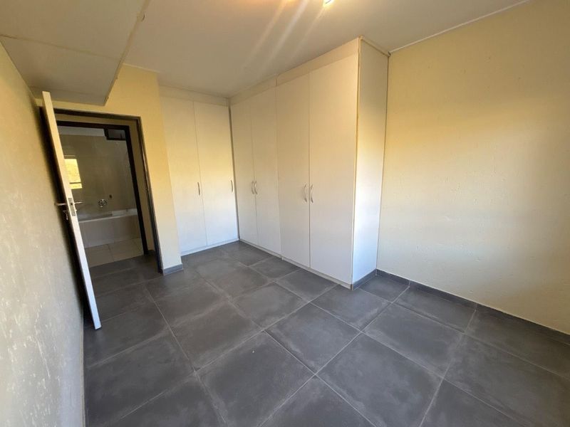 A vacant bedroom featuring built-in cupboards, large format floor tiles, and direct access to an en-suite bathroom.