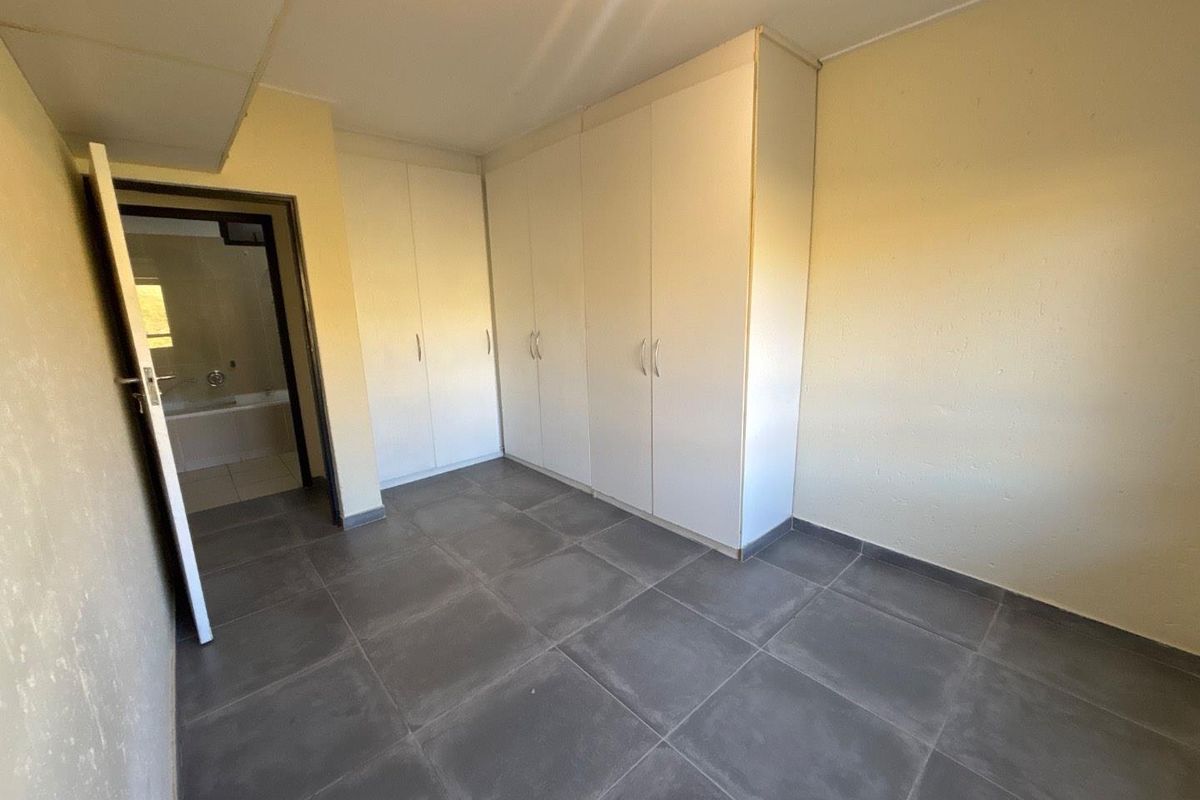 A vacant bedroom featuring built-in cupboards, large format floor tiles, and direct access to an en-suite bathroom.