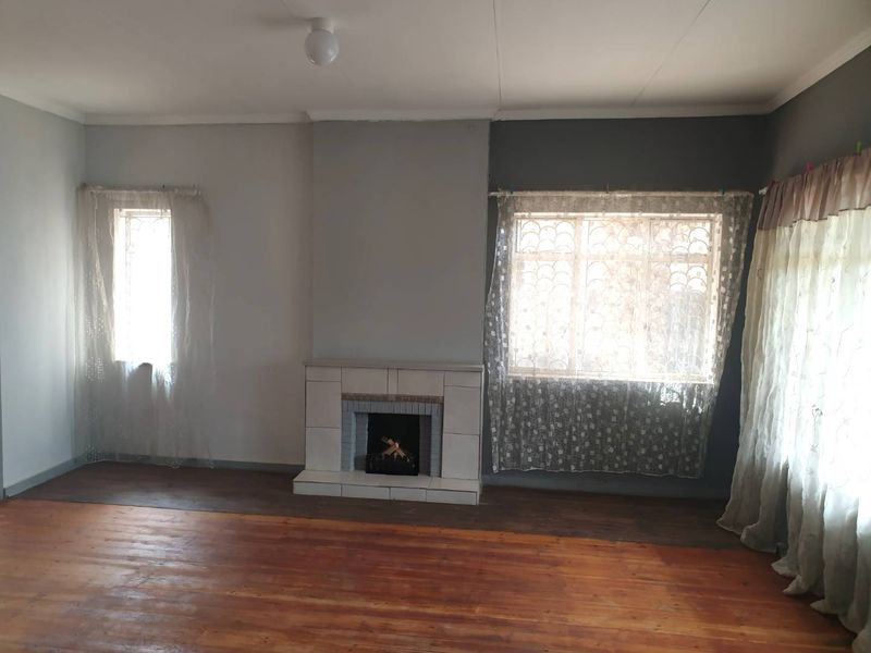 A spacious living room featuring original hardwood flooring, a central tiled fireplace, and large windows with security bars.