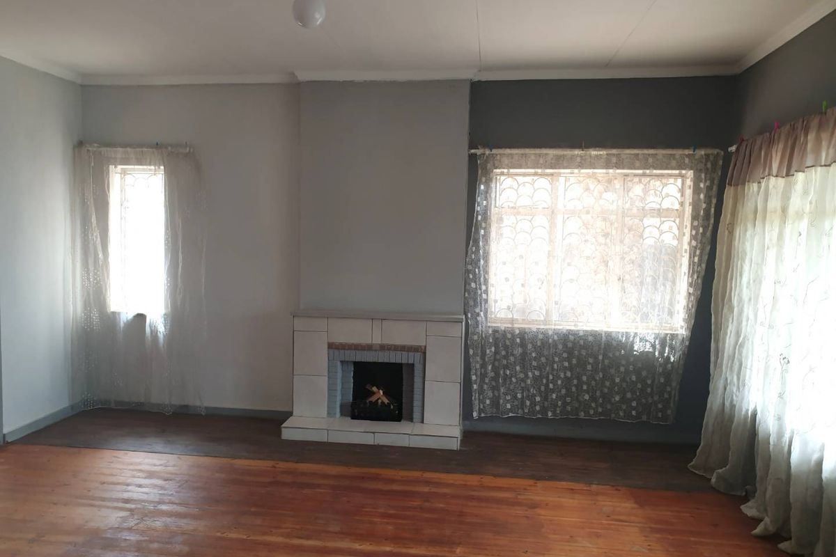 A spacious living room featuring original hardwood flooring, a central tiled fireplace, and large windows with security bars.