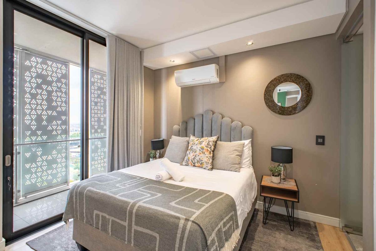 Modern bedroom featuring floor-to-ceiling sliding glass doors, integrated air conditioning unit, and access to a private balcony with decorative privacy screening.