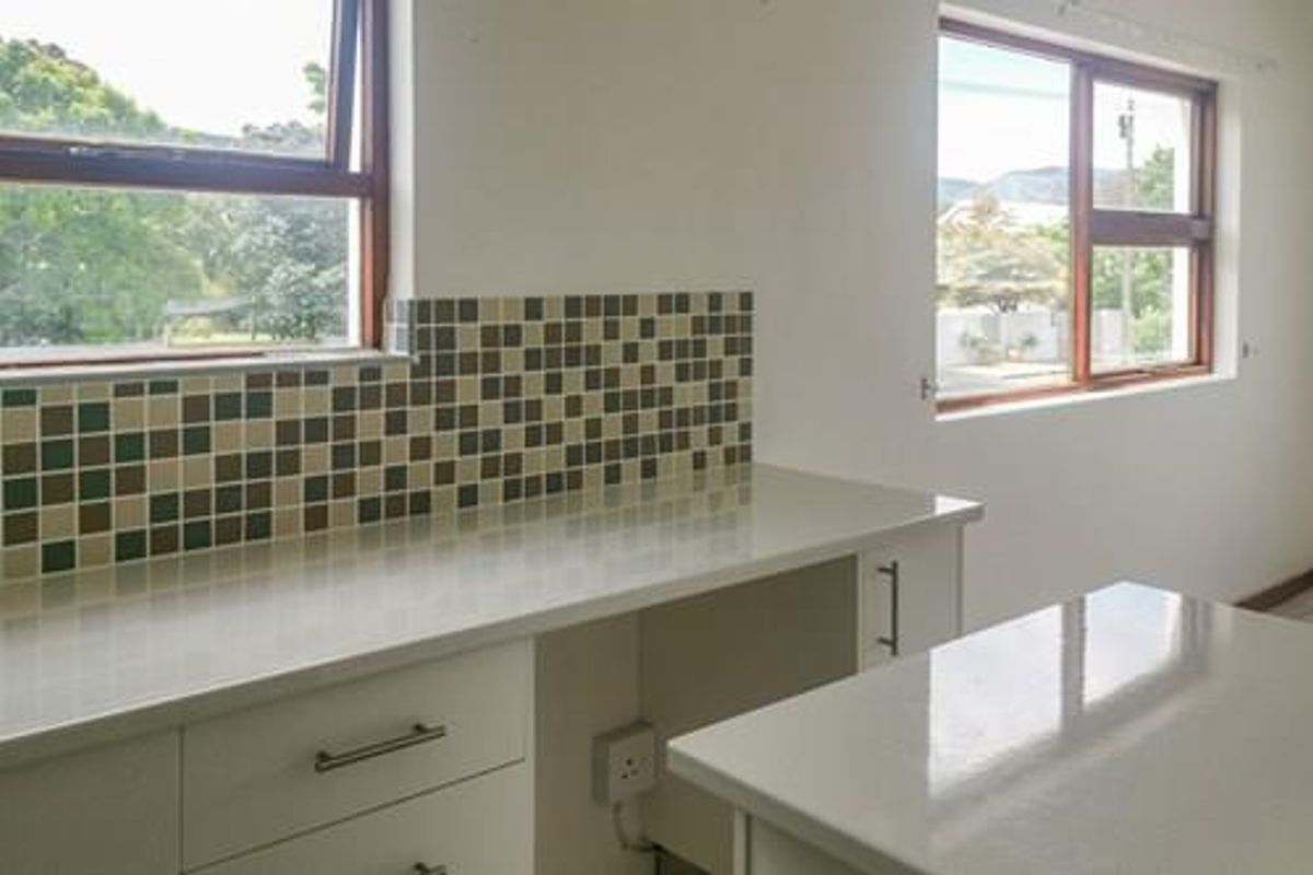 A bright, empty kitchen area featuring modern quartz countertops, mosaic tile backsplash, and ample built-in cabinetry with natural light from dual windows.