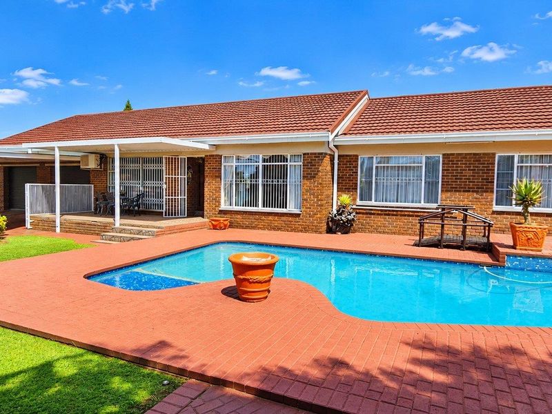 Rear exterior view featuring a swimming pool, brick-paved patio area, and a well-maintained brick house with a tiled roof.