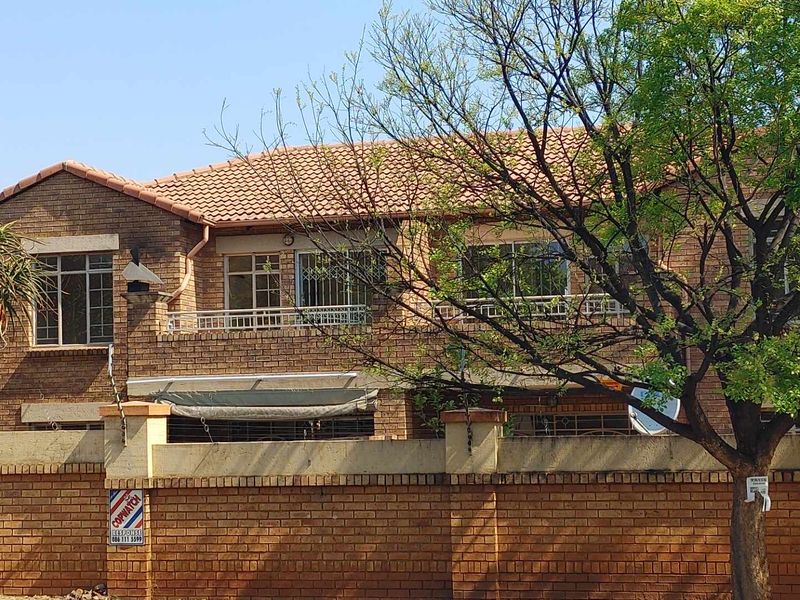 Front elevation of a double-story face brick townhouse featuring a tiled roof, security bars on windows, and a private brick-walled boundary.