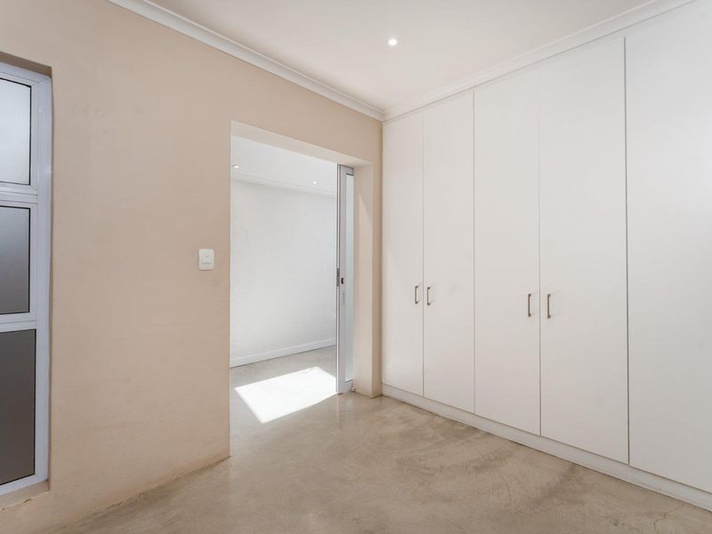 A clean, empty bedroom featuring neutral walls, polished concrete flooring, and extensive built-in white cabinetry with a sliding door leading to an adjacent room.