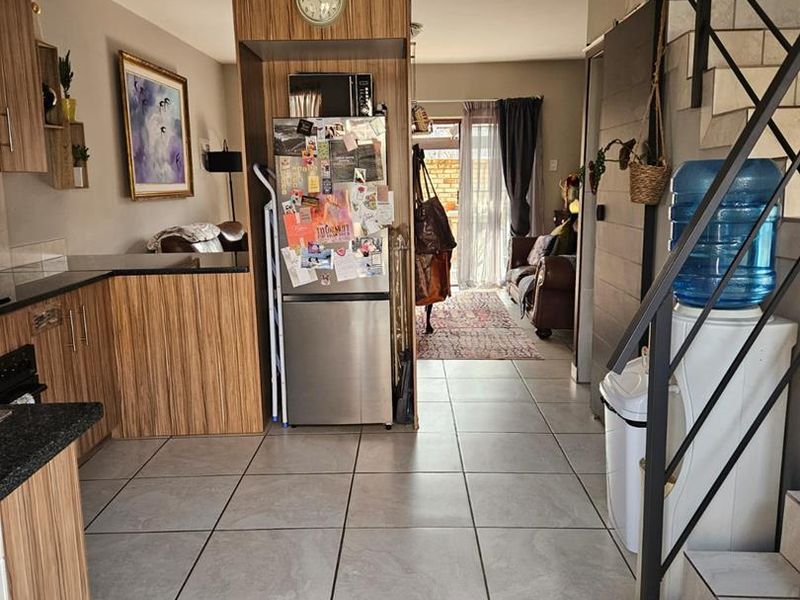 Open-plan living area featuring tiled floors, a kitchen with wood-look cabinetry and granite countertops, and a staircase leading to the upper level.