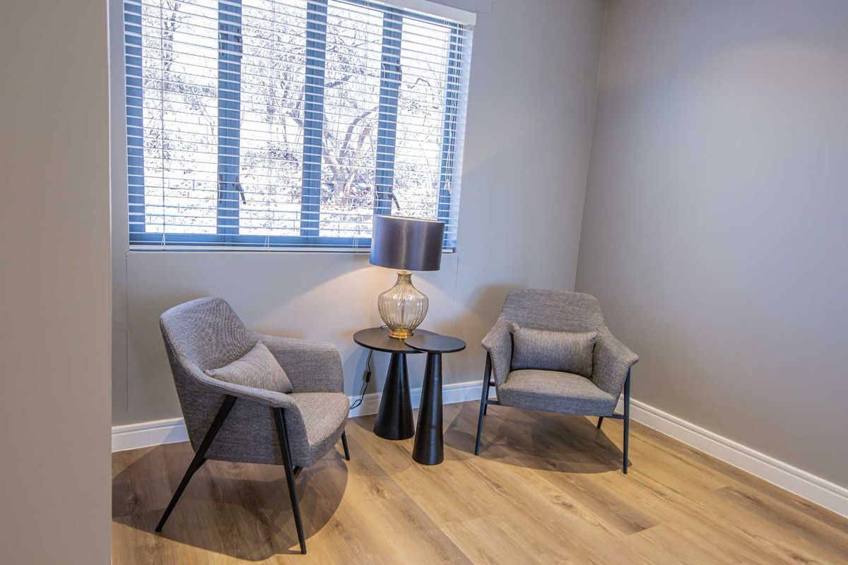 A bright, neutral living space featuring modern wood-look flooring and a large window with fitted blinds, offering a clean and versatile area.